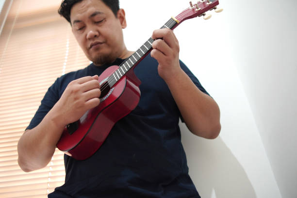 istock Asian man playing ukulele at home 2187229494