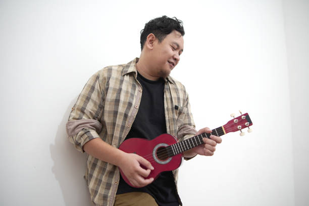 istock Asian man playing ukulele at home 2187230416