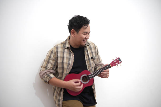 istock Asian man playing ukulele at home 2187230427