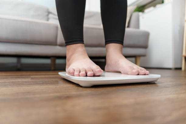istock Fat diet and scale feet standing on electronic scales for weight control. Measurement instrument in kilogram for a diet control. 2187241211
