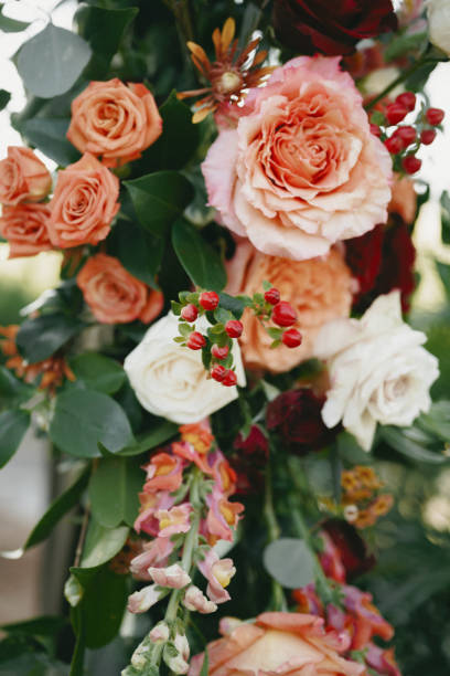 A close-up of a beautifully arranged wedding ceremony arch adorned with orange, white, and red roses, snapdragons, and lush greenery. Captured during a backyard wedding in Savannah, this floral design adds a romantic and elegant touch to the special day