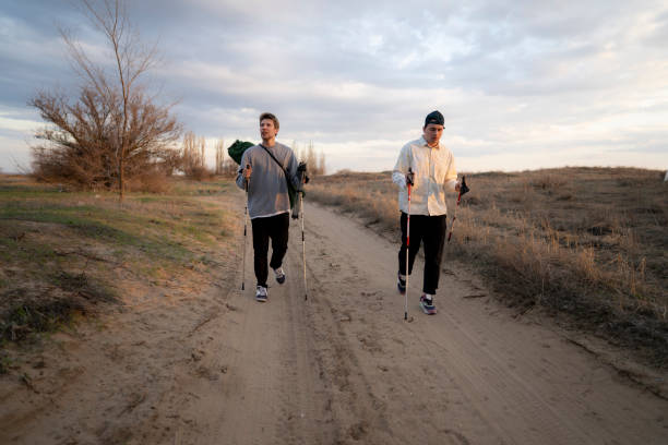 istock Two men hike along a sandy path through a pine forest at sunset. The men are wearing casual clothing and carrying hiking poles 2187249200