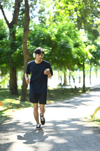 istock Young asian man with headphone jogging through a lush green park 2187250238