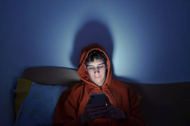 adolescente usando smartphone sentado na cama à noite - meninos adolescentes - fotografias e filmes do acervo