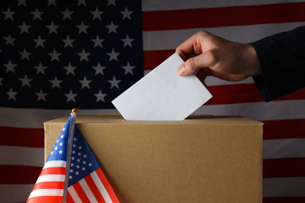 istock Paper voting box with paper and hand on american flag background 2187255656