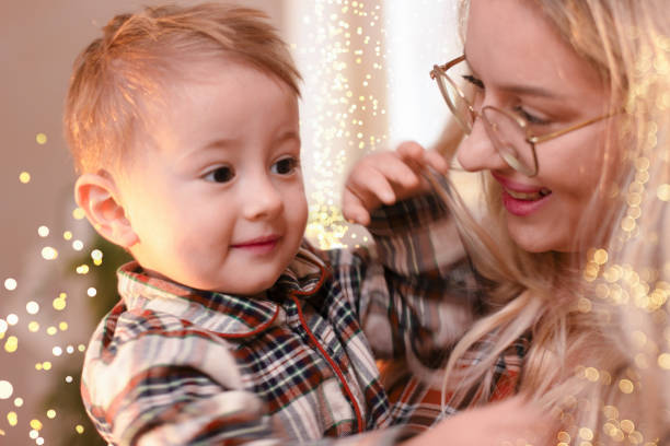 Portrait of a young woman in glasses and a small one and a half year old child. Mother looks lovingly at the baby, smiling