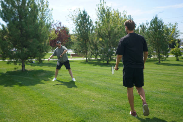 istock Two individuals engage in a friendly badminton match on a lush green lawn, surrounded by trees under a clear blue sky on a beautiful summer day 2187258582