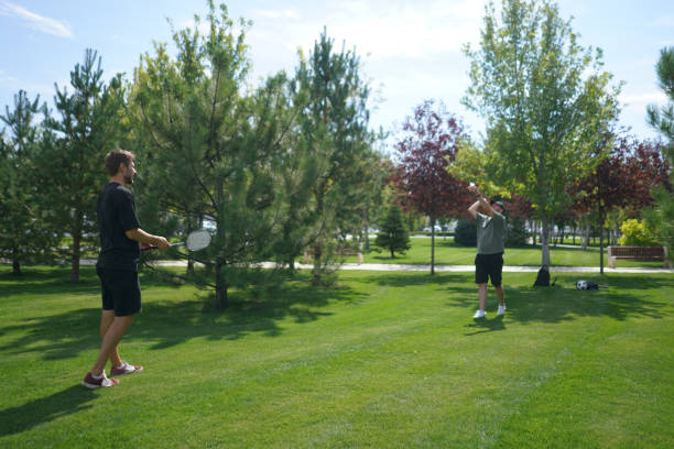 istock Two individuals engage in a friendly badminton match on a lush green lawn, surrounded by trees under a clear blue sky on a beautiful summer day 2187258585