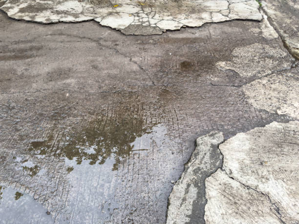 istock Damaged concrete pavement with visible cracks and small puddles 2187263960