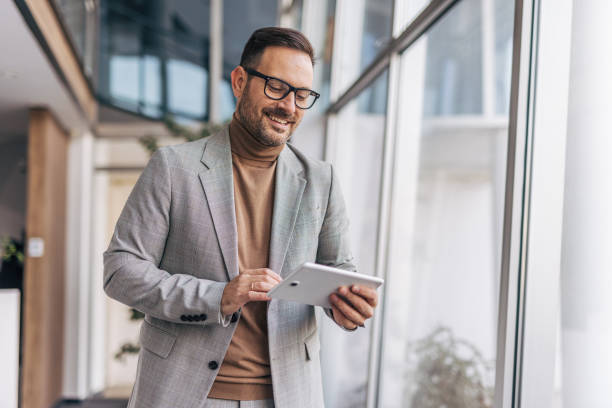 istock A smiling businessman is using a digital tablet while standing in an office corridor 2187264801