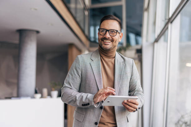 istock A smiling businessman is using a digital tablet while standing in an office corridor 2187264820