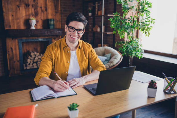 istock Young man enjoying leisure time indoors while jotting ideas in notebook next to modern laptop in stylish loft apartment 2187265501