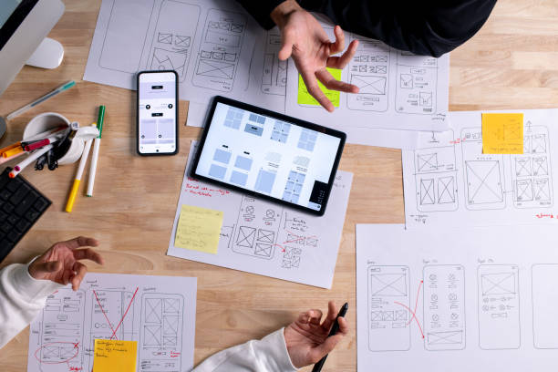 istock UX UI designers discussing and brainstorming on wireframes for a website and mobile app prototype, surrounded by sketches of user flow and design tools, in the concept of website and mobile application design concept. 2187265533