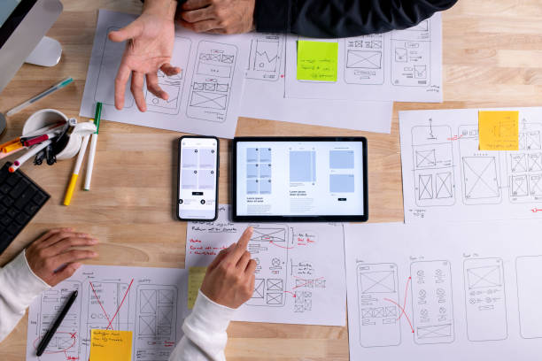istock UX UI designers discussing and brainstorming on wireframes for a website and mobile app prototype, surrounded by sketches of user flow and design tools, in the concept of website and mobile application design concept. 2187265534