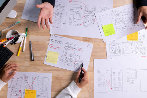 istock UX UI designers discussing and brainstorming on wireframes for a website and mobile app prototype, surrounded by sketches of user flow and design tools, in the concept of website and mobile application design concept. 2187265541