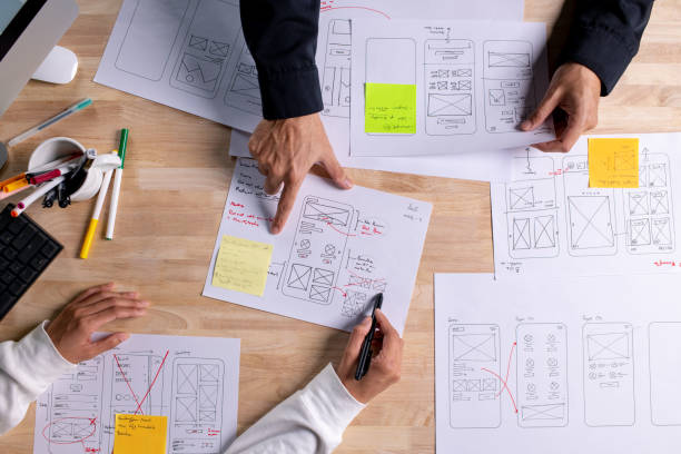 istock UX UI designers discussing and brainstorming on wireframes for a website and mobile app prototype, surrounded by sketches of user flow and design tools, in the concept of website and mobile application design concept. 2187265542