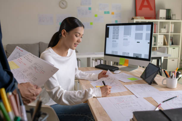 istock UX UI designers discussing and brainstorming on wireframes for a website and mobile app prototype, surrounded by sketches of user flow and design tools, in the concept of website and mobile application design concept. 2187265558