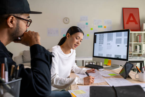 istock UX UI designers discussing and brainstorming on wireframes for a website and mobile app prototype, surrounded by sketches of user flow and design tools, in the concept of website and mobile application design concept. 2187265559