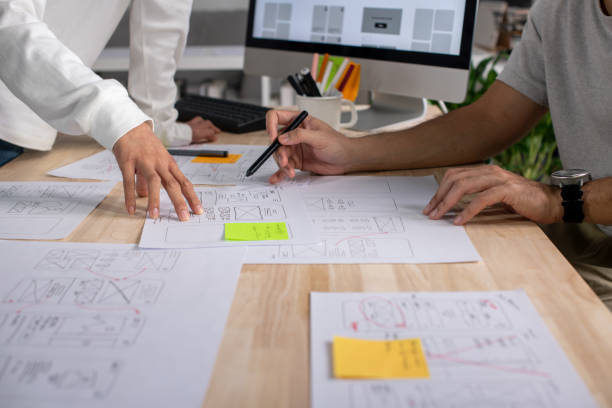 istock UX UI designers discussing and brainstorming on wireframes for a website and mobile app prototype, surrounded by sketches of user flow and design tools, in the concept of website and mobile application design concept. 2187265641
