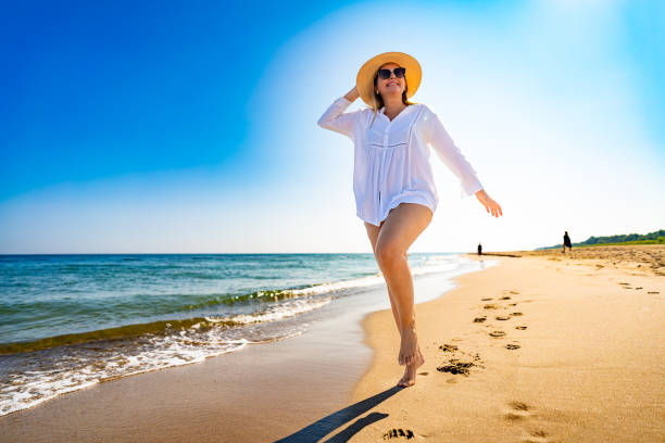 istock Beautiful mature woman walking on sandy beach. Front view 2187267369