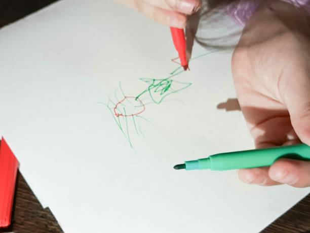 istock The child's hand draws, paints with a red felt-tip pen on paper on the children's Development table. Children's drawings. 2187268109