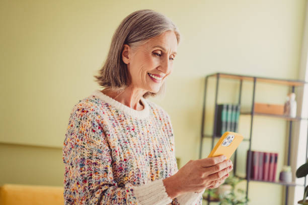 istock Charming mature woman smiling while using smartphone in cozy living room during daylight, embracing tranquility and joy. 2187269666