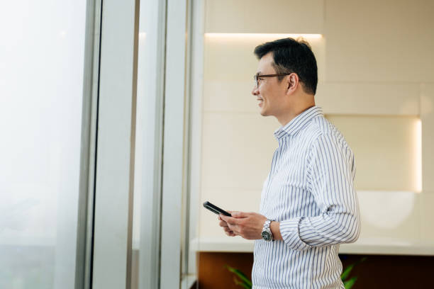 istock Asian businessman holding smartphone in office. Middle aged manager using cell phone mobile app. Digital technology application and solutions for business. 2187270502