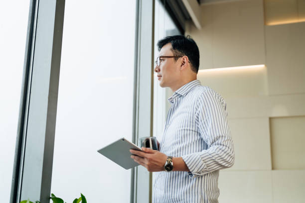 istock Confidence Asian businessman holding a digital tablet and looking through window. 2187270507