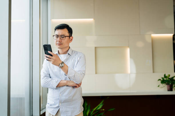 istock Asian businessman holding smartphone in office. Middle aged manager using cell phone mobile app. Digital technology application and solutions for business. 2187270510