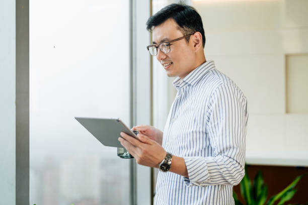 istock Confidence Asian businessman holding a digital tablet and looking through window. 2187270514