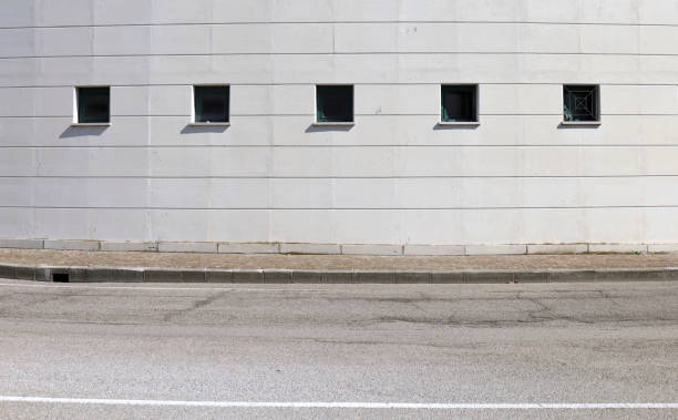 istock White painted concrete facade with a row of small windows. Sidewalk and street in front 2187272749