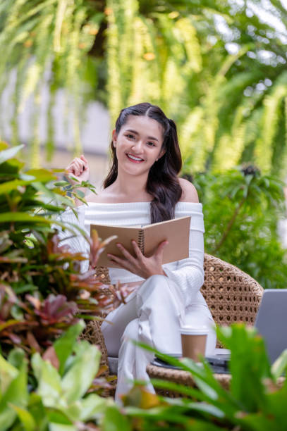 istock Young woman working remotely using a laptop and taking notes in a notebook Think and come up with project ideas in a relaxed atmosphere at an outdoor cafe. 2187277767