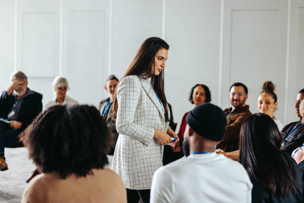 A facilitator leads a questions and answers session with a diverse audience, fostering engagement and discussion in a bright room.