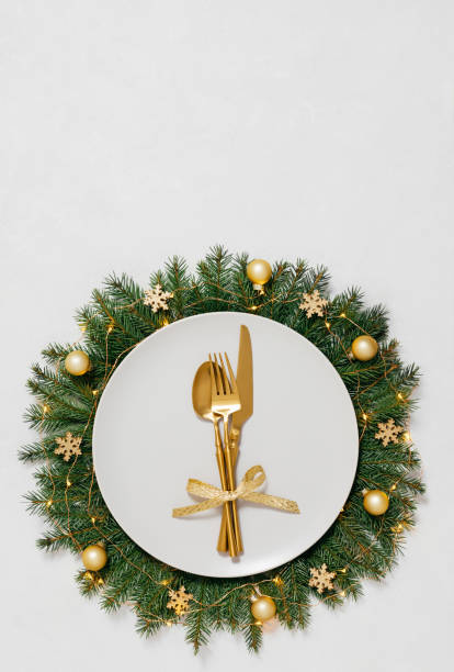 istock Festive table setting with gold cutlery and Christmas wreath on white background with copy space. New Year serving. Vertical orientation. 2187279269