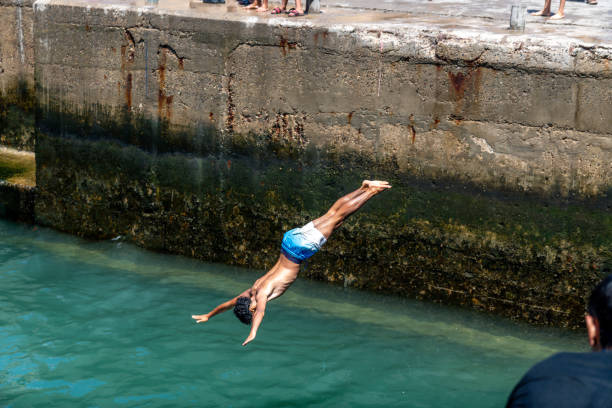 Acre, Israel - August 3, 2016: Young man jumps to the sea from the top of the ancient walls of Acre, Israel. Acre is one of the oldest continuously inhabited sites in the world