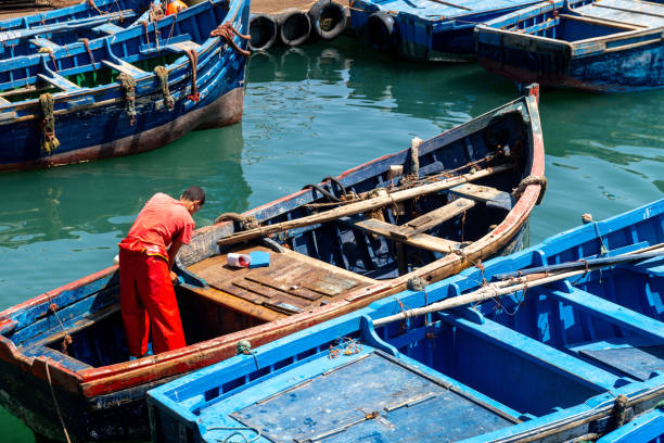 Essaouira Marokko 29.07.2024: Fisherman in a blue boat, busy with repairs and preparations, other boats in the water.