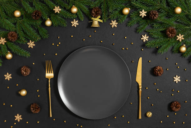istock A black empty plate with gold cutlery and Christmas decorations on black background. Empty white plate for New Year serving. Top view, flat lay. 2187281178