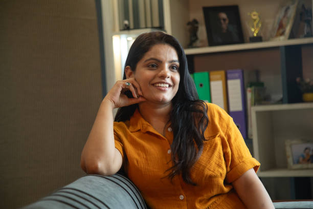 Smiling beautiful young woman contemplating and looking away while relaxing on sofa in living room