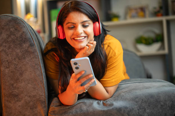 Happy young woman using smart phone on sofa at home