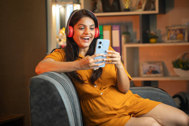 istock Happy young woman using smart phone on sofa at home 2187286401