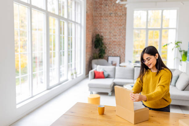 istock Woman eagerly opening box in sunlit modern living space. 2187288003