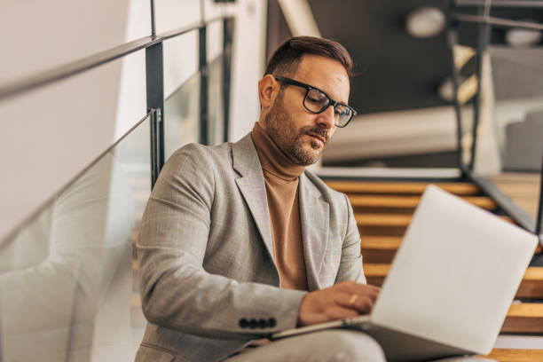 istock A close-up of a businessman using a laptop while sitting on indoor stairs 2187299780