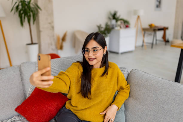istock Smiling woman on sofa taking a selfie with phone. 2187302077