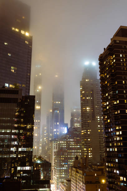Stunning cityscape view of illuminated high-rise buildings shrouded in fog at night.