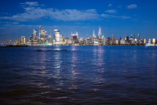 Stunning night view of modern city skyline with illuminated skyscrapers and their reflections shimmering on a calm body of water.