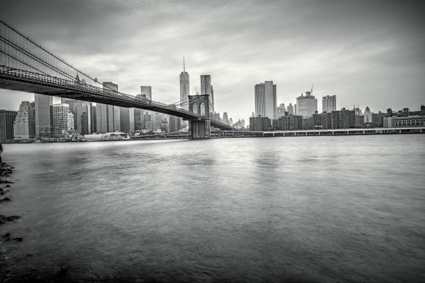A stunning black and white photograph showcasing the iconic Brooklyn Bridge and Manhattan skyline, taken from across the river.