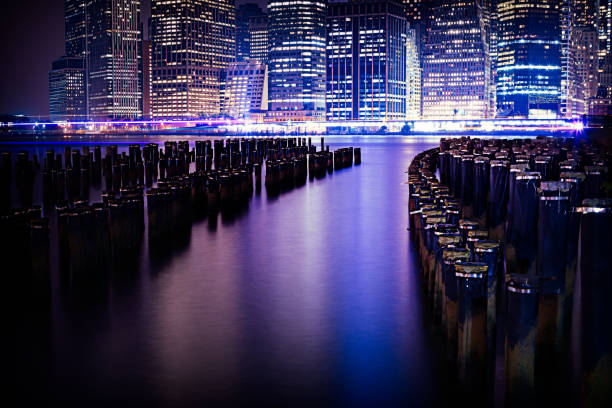 A mesmerizing night cityscape featuring illuminated skyscrapers and their reflections in calm water with silhouetted wooden beams.