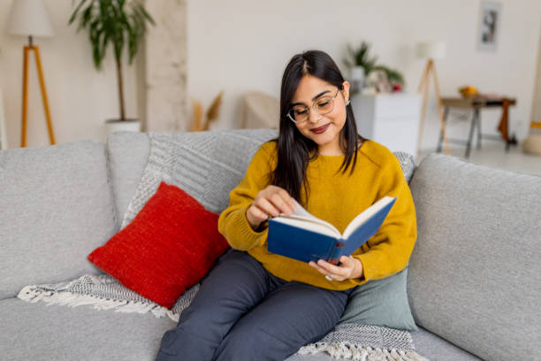 istock Woman in yellow sweater reads on modern gray sofa 2187304876