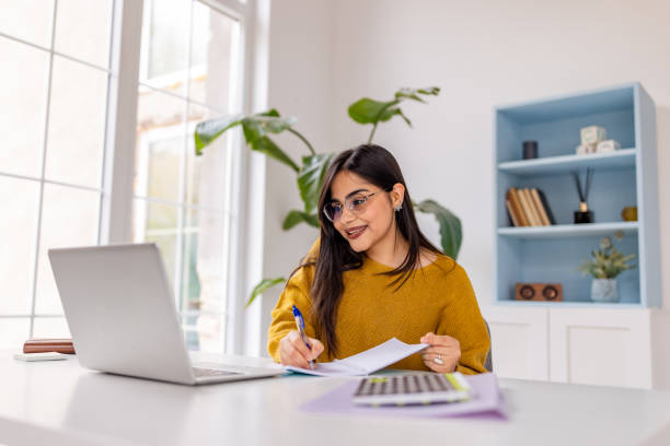 istock Woman Smiling While Writing at Desk with Laptop 2187305979