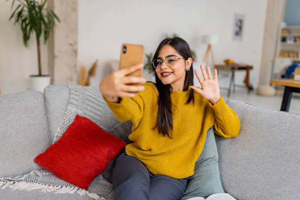 istock Woman waving while taking selfie on a comfortable couch. 2187306375